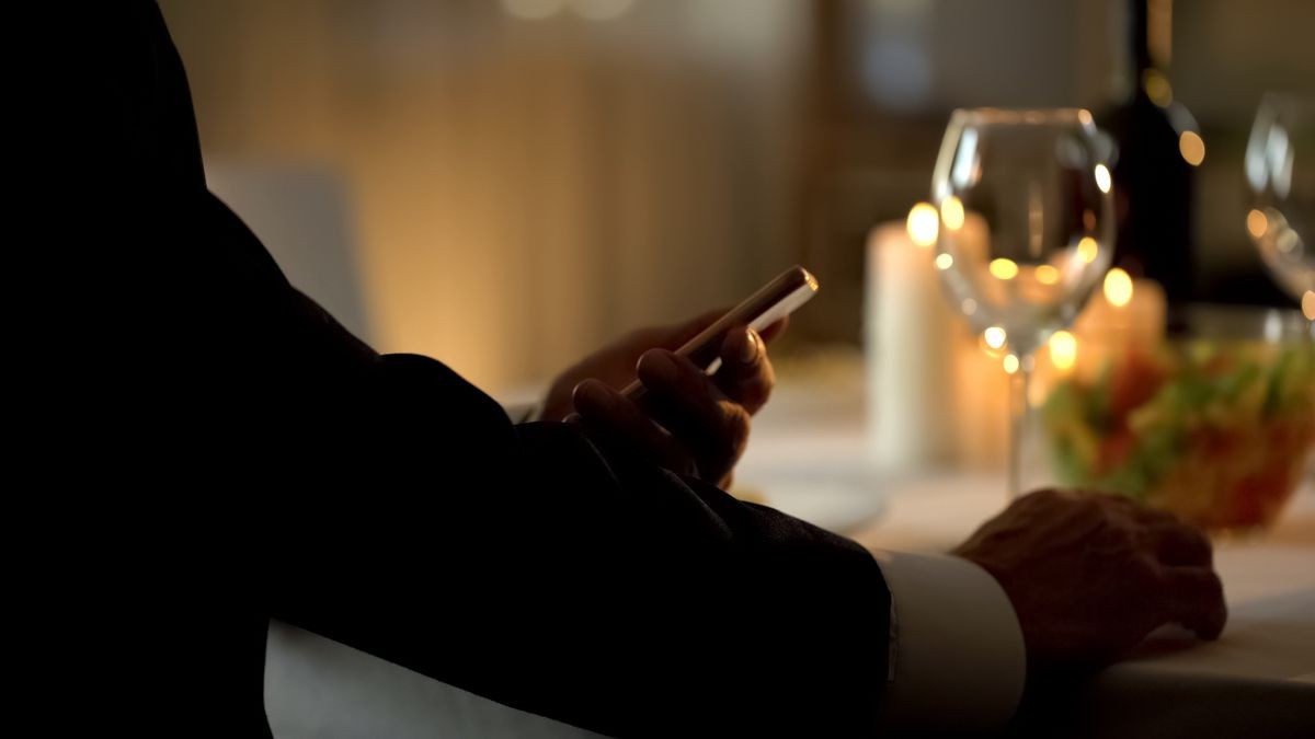 Elegant male scrolling smartphone application, waiting for date in restaurant